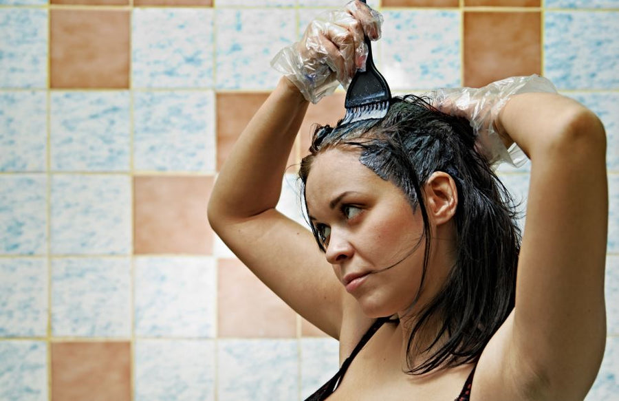 Woman wearing gloves applies Bigen hair color at home with brush, tile background